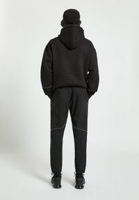 Svart hoodie och taperade byxor, med kontrasterande vit sömnad och sidofickor. Bärs med en matchande svart bucket hat och sneakers.