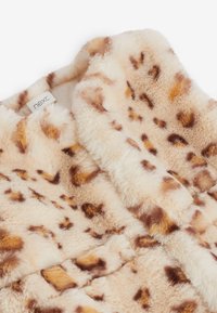 Fuskpälsjacka i ljusbeige med bruna leopardfläckar, med mjuk textur och vikbar krage. Branded etikett är synlig inuti.
