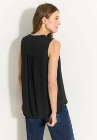 Zwarte mouwloze top van lichtgewicht stof, met een plooidetail aan de achterkant en een ontspannen pasvorm, gecombineerd met blauwe denim jeans.