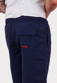 Tengerészkék rövidnadrág rugalmas derékkal. Jellemzői közé tartozik egy hátsó zseb és egy piros hímzett "USPA" logó.