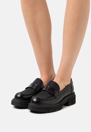 Black leather loafers with a textured grey fabric panel and a thick, ridged sole; feature a wide strap across the top.