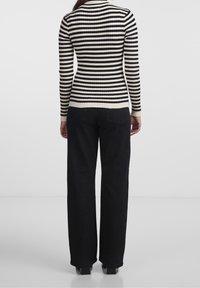 Czarny i kremowy sweter w prążki z długimi rękawami, dopasowanym krojem i wysokim kołnierzem. W połączeniu z luźnymi czarnymi spodniami.