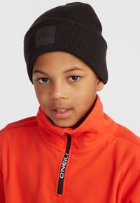 Black ribbed knit beanie with a logo patch, worn by a person in a bright orange fleece pullover with a zip collar and black zipper.