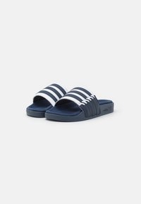 Navy blue slide sandals with three white striped bands, soft textured upper, and a cushioned sole. Features brand logo on outer side.