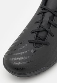 Scarpa sportiva nera con un design liscio e affusolato. Presenta motivi superficiali testurizzati e lacci neri, con un logo discreto sul lato.