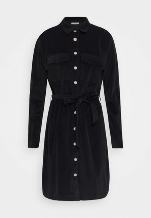 Black long-sleeve shirt dress with beige buttons down front, chest flap pockets, collar, and matching fabric belt tied at waist.