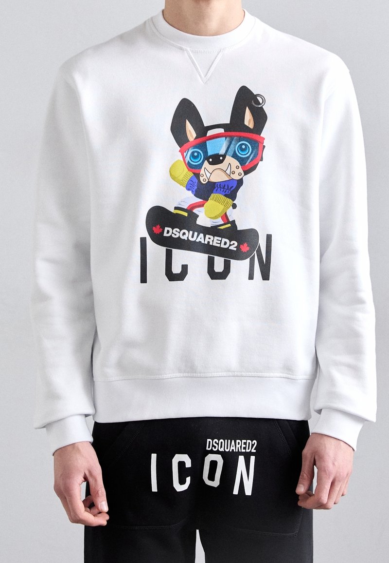 Sweat-shirt blanc avec un chien de dessin animé coloré portant des lunettes de ski sur un snowboard au-dessus du mot "ICON" et un pantalon noir avec le texte "DSQUARED2 ICON".