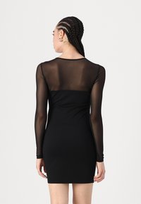 Rochie neagră cu un corp mulat, mâneci lungi din material transparent și un corp solid. Textură netedă cu un design minimalist și decolteu rotund.
