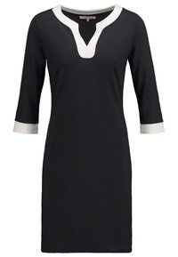 Robe noire longueur genou avec manches trois-quarts, bordure d'encolure en V blanche et poignets de manches blancs.