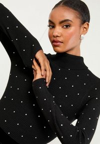 Czarny sweter z golfem, prążkowany, ozdobiony białymi, perłowymi detalami, z długimi rękawami i dopasowanym krojem.