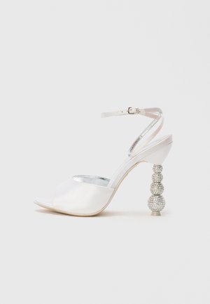 Hvide satin åbne tå højhælede sandaler med ankelrem og en funklerende perledekoreret hæl med tre runde elementer.