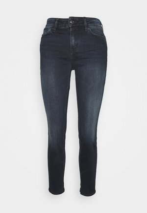 Jeans skinny a lavaggio scuro con chiusura frontale con bottone e cerniera, cinque tasche e leggero sfumato su cosce e ginocchia.
