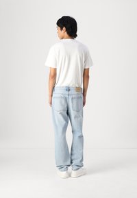 T-shirt blanc et jeans en denim bleu clair. Jeans à coupe décontractée avec deux poches arrière, étiquette sur la taille et baskets blanches.