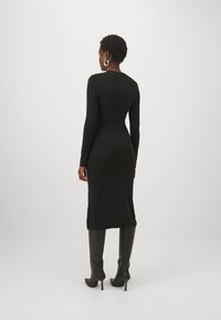 Melnas garām piedurknēm kleita, izgatavota no elastīga materiāla, pieguļoša silueta, līdz ceļgaliem, apvienota ar melniem zābakiem uz papēžiem, gluda tekstūra.