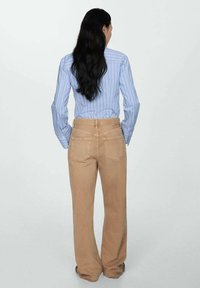 Pantaloni beige a gamba larga con vita alta e cuciture in evidenza. Abbinati a una camicia a righe blu e bianche, visti da dietro.