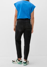 Czarne jeansy z wysokim stanem i prostą nogawką, w połączeniu z niebieską bluzką z krótkim rękawem. W zestawie czarno-białe trampki z zielonymi akcentami.