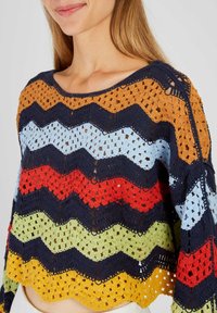 Sweter na szydełku z wzorem zygzakowym w odcieniach niebieskiego, czerwonego, zielonego, pomarańczowego i żółtego. Luźny krój z otwartą strukturą i szerokim dekoltem.
