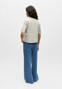 Haut gris clair à manches courtes avec une silhouette carrée, associé à un jean en denim bleu taille haute à jambes larges. Design simple, texture lisse.