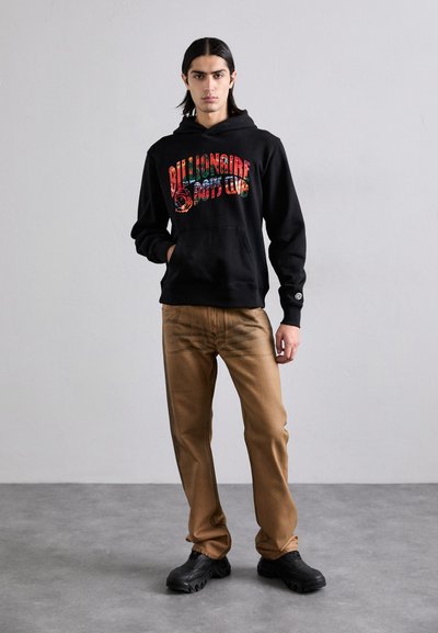 Haut à capuche noir avec un graphisme multicolore "Billionaire Boys Club". Associé à un pantalon beige et des chaussures noires imposantes. Texture lisse.