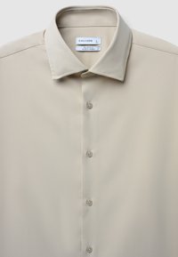 Camicia slim-fit beige con colletto, caratterizzata da una texture liscia e cinque bottoni, etichettata 'CALLIOPE', taglia L.