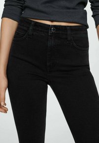 Jeans negros de cintura alta de denim, con cierre de botón frontal, dos bolsillos delanteros y una textura suave. Vista en primer plano.