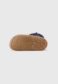 Soletta di scarpa blu scuro con una suola in gomma arancione e marrone texturizzata, caratterizzata da pattern zigzag e circolari; nome del marchio impresso.