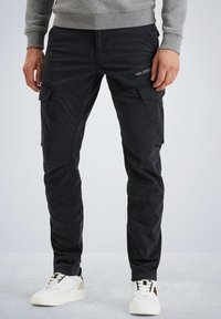 Schwarze Cargo-Hosen mit mehreren Taschen, schmalem Schnitt und sichtbaren Nähten; kombiniert mit weißen Sneakers und einem grauen Sweater.