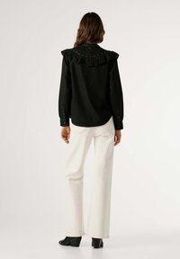 Čierna rifľová košeľa s volánovým golierom a korálkovými ozdobami, kombinovaná s bielymi širokými nohavicami a čiernymi členkovými čižmami na podpätku. Jemná textura a dizajnové detaily.