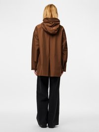 Καφέ αδιάβροχο μπουφάν με κουκούλα και άνετη εφαρμογή, με ομαλή υφή. Συνδυάζεται με μαύρο παντελόνι φαρδιάς γραμμής. Απλός σχεδιασμός, χωρίς εμφανή σχέδια.