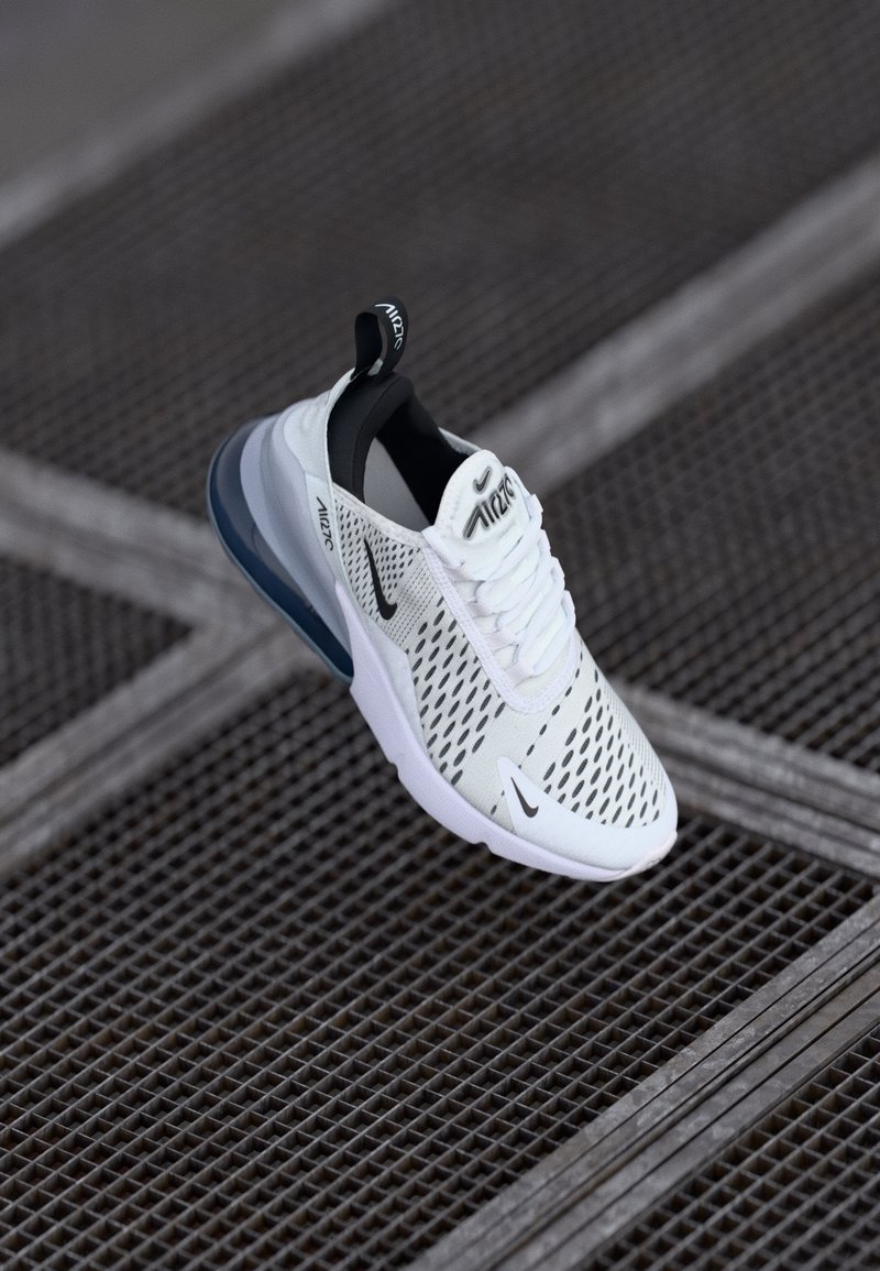 Weißer Sportschuh mit einem Obermaterial aus Mesh, schwarzen Akzenten und einer sichtbaren Luftpolsterung in der Sohle. Verfügt über ein Schnürdesign und eine Zuglasche.