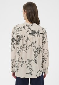 Langærmet beige bluse med sort blomsterprint, med en samlet bagsøm og et blødt, tekstureret stof.