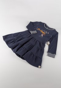 Marineblaues Langarmkleid mit Rüschenschichten, das ein orange-weißes "Es ist Magie"-Motiv, gestreifte Bündchen und ein Etikett am Saum hat.