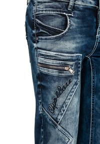 Dunkelblaue Denim-Jeans mit verblassten Bereichen, mehreren Taschen, einer Reißverschlusstasche und gesticktem Logo-Detail an der Seite.