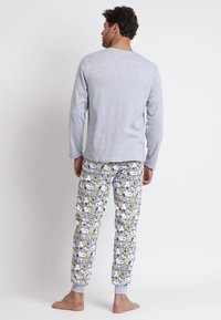 Top de manga larga gris claro combinado con pantalones de pijama blancos que presentan patrones de perros de dibujos animados y acentos amarillos. Tejido suave con puños acanalados.
