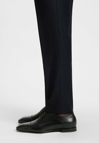 Black leather dress shoes with a sleek design, featuring a pointed toe and lace-up closure, paired with tailored black trousers.
