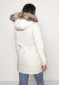 White puffer coat featuring a fur-lined hood, drawstring waist, and smooth texture. The back shows the length covering the hips.