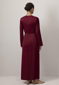 Pikad burgundia värvi kleit, millel on pikad varrukad ja kehakohene talje. Sile tekstuur, lukuga sulgemine seljaosas ja põrandani ulatuv disain.