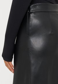 Fekete bőr szoknya, sima textúrával,ígyell szabással és magas derékkal. Oldalsó cipzár részlet látható, elegáns kivitelezéssel.