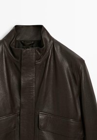 Giacca di pelle marrone con colletto alto, due tasche frontali e superficie liscia, che mette in mostra un design minimalista e linee pulite.