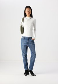 Balta ribota gara piedurkņu krekls ar izliekta dizaina elementiem, gaiši zili džinsi un melni augstpapēžu apavi ar spīdīgu pirkstu detaļu. Zaļa pleca soma.