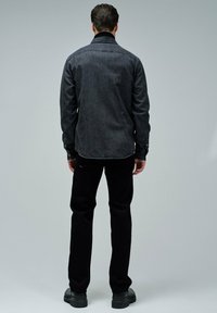 Camisa de mezclilla negra con cuello puntiagudo, mangas largas y cierres de botón; combinada con pantalones negros y botas negras resistentes.