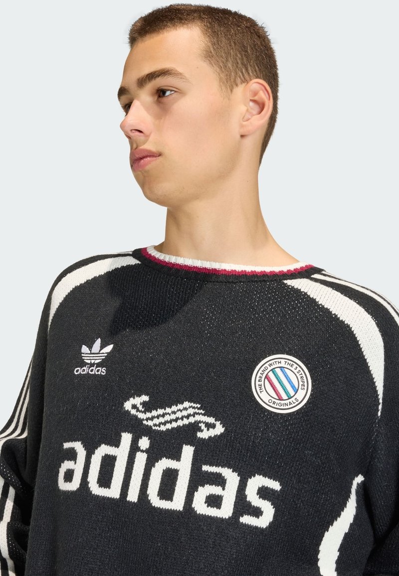 Black knitted sweater with white stripes and "adidas" logo. Features a round neck and circular badge with colored stripes.