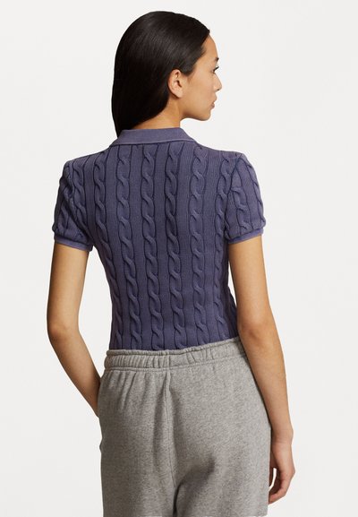 Polo violet à manches courtes avec texture en tricot à chevrons, doté d'un col et d'une coupe ajustée, associé à un pantalon gris avec ceinture élastique.