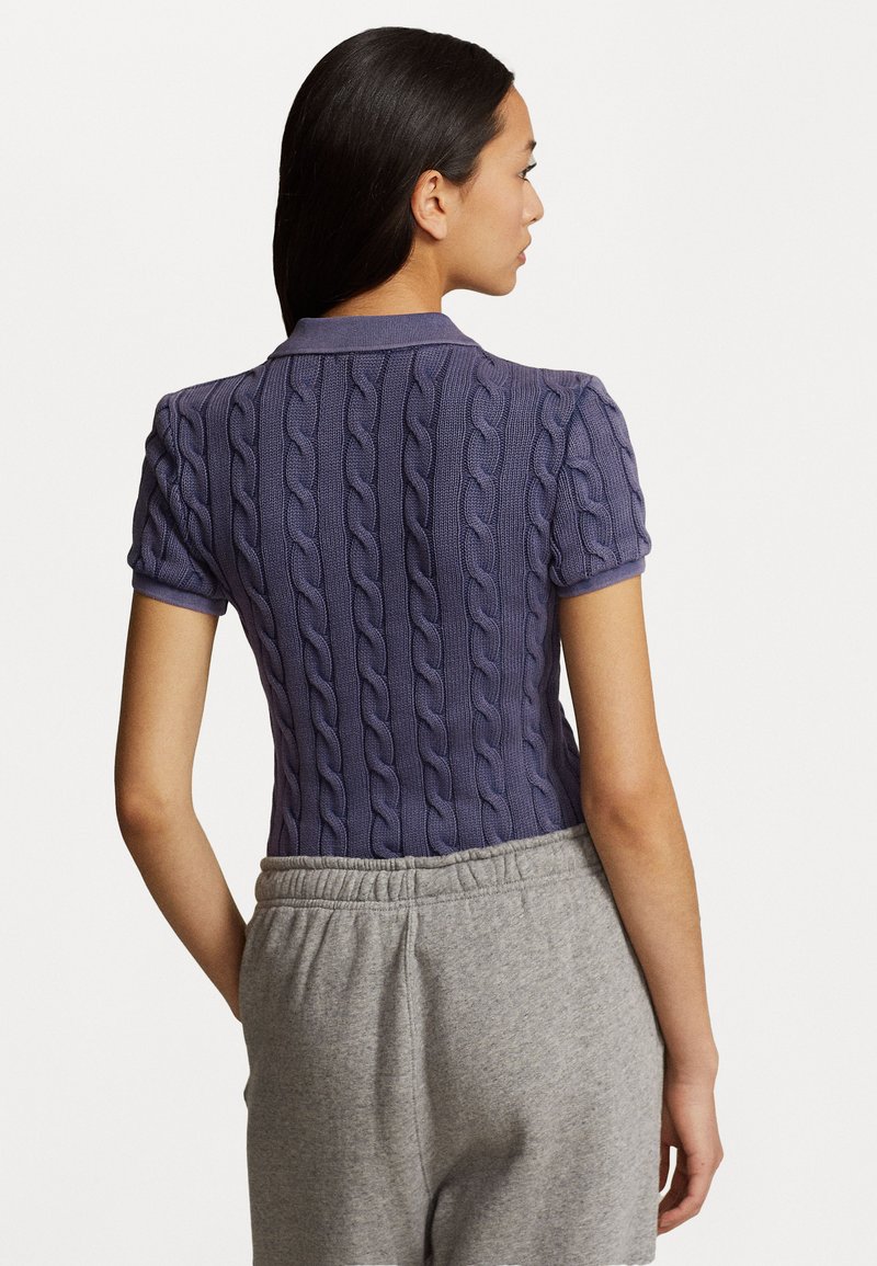 Polo corto viola a maniche corte con texture a treccia, dotato di colletto e design aderente, abbinato a pantaloni grigi con vita elastica.