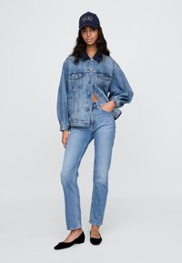 Jeans jakna s kratkim krojem, svetlo modre barve, z žepki na prsih, kombinirana z modrimi jeans hlačami in črnimi ravnimi čevlji, dopolnjena z mornarsko kapo.