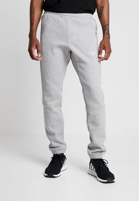 Grå träningsoverallsbyxor i mjukt, strukturerat tyg med resårlinning, sidfickor och en subtil logo på vänster lår.