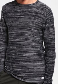 T-shirt à manches longues gris avec un motif rayé texturé. Comprend un col rond et une petite étiquette de marque discrète à l'ourlet.