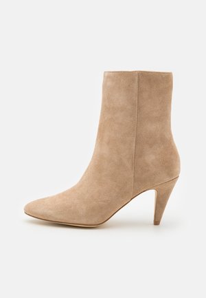Bottine en suède beige avec un bout pointu et un talon conique de hauteur intermédiaire, présentée de profil sur un fond blanc uni.