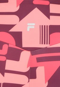 Tela de baño multicolor con patrones geométricos en rosa, marrón y blanco. Incluye detalles de logotipo y líneas de costura en contraste.