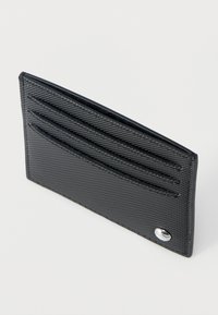 Λεπτή μαύρη θήκη καρτών με υφή, διαθέτει τρεις θέσεις για κάρτες και ένα μικρό στρογγυλό ασημένιο έμβλημα στην κάτω δεξιά γωνία.